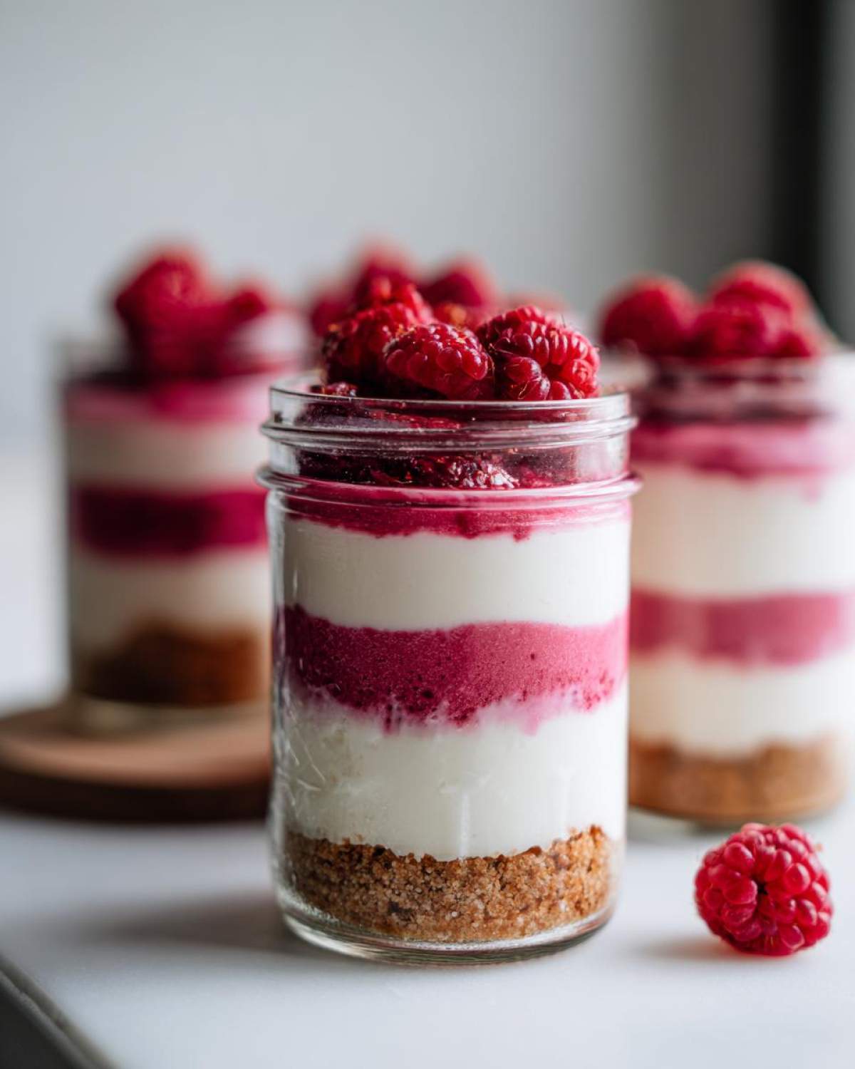 Close-up of No-Bake Raspberry White Chocolate Cheesecake Jars showing graham cracker crust, white filling, and raspberry layers topped with fresh raspberries.