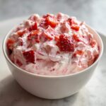 A close-up shot of creamy No-Bake Strawberry Cheesecake Dip mixed with chunks of fresh strawberries in a white bowl.