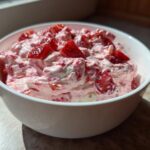 A white bowl filled with creamy, pink No-Bake Strawberry Cheesecake Dip topped with fresh strawberry chunks.