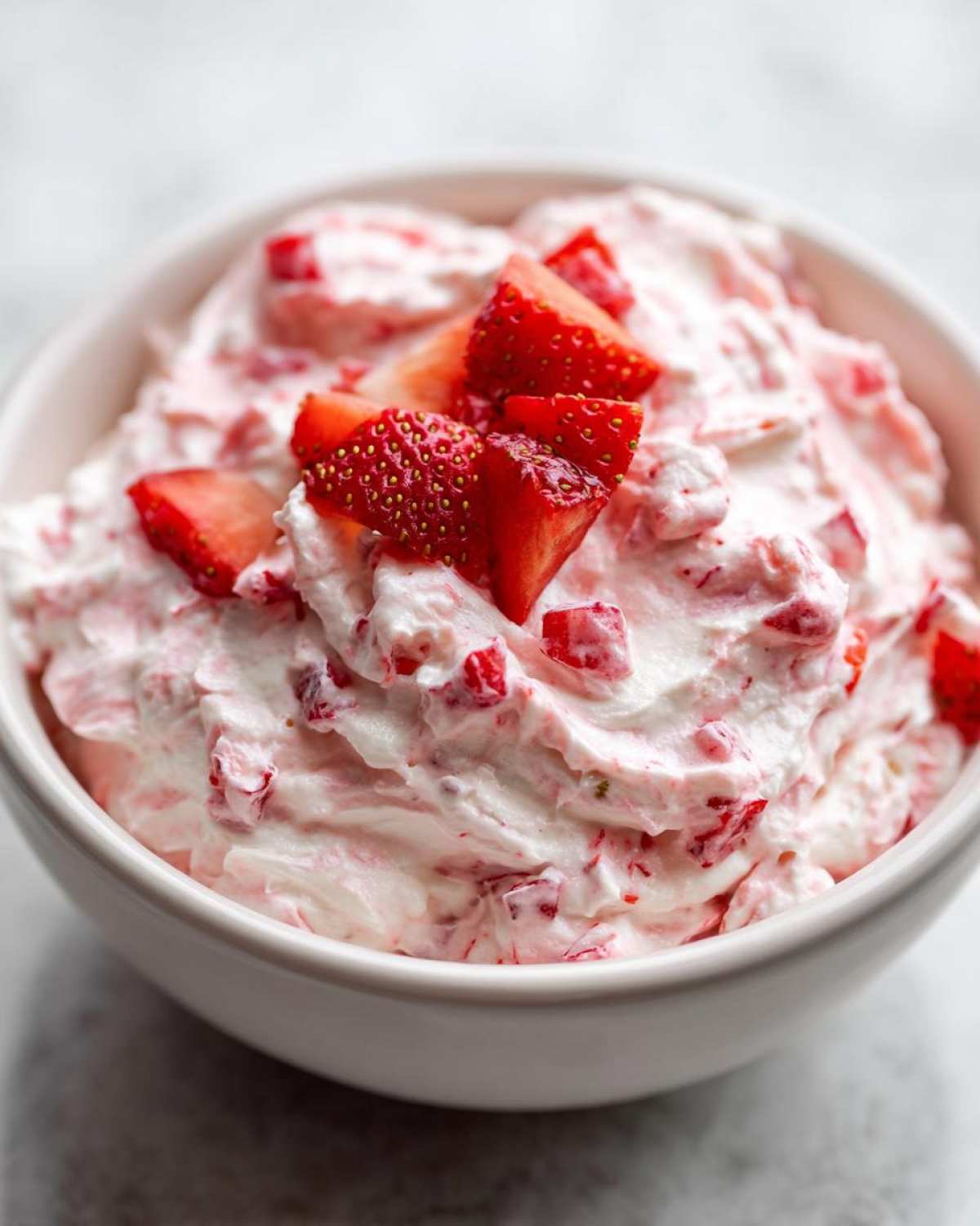 A close-up view of creamy No-Bake Strawberry Cheesecake Dip mixed with diced strawberries, topped with fresh strawberry pieces.