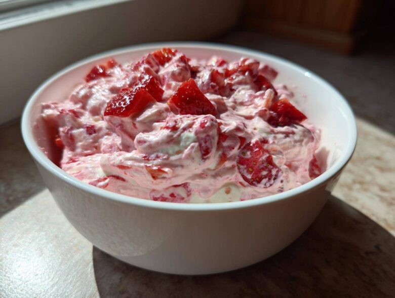 A white bowl filled with creamy, pink No-Bake Strawberry Cheesecake Dip topped with fresh strawberry chunks.