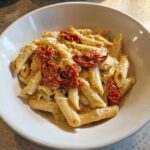 A close-up of One-Pot Creamy Goat Cheese Pasta with penne coated in sauce and topped with roasted tomatoes.