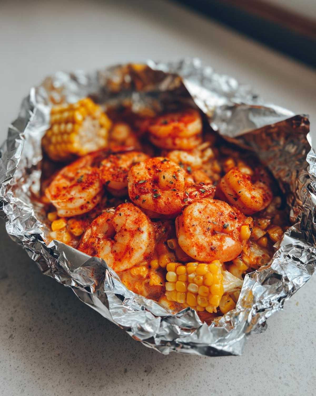 Close-up of cooked shrimp and corn on the cob in a foil packet, seasoned with Cajun spices.