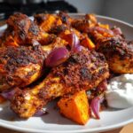 Close-up of spicy Sheet Pan Harissa Chicken with sweet potatoes and red onions served with a dollop of yogurt.