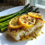 A perfectly cooked fillet of Sheet Pan Lemon Herb Cod with Asparagus, topped with lemon slices and herbs.