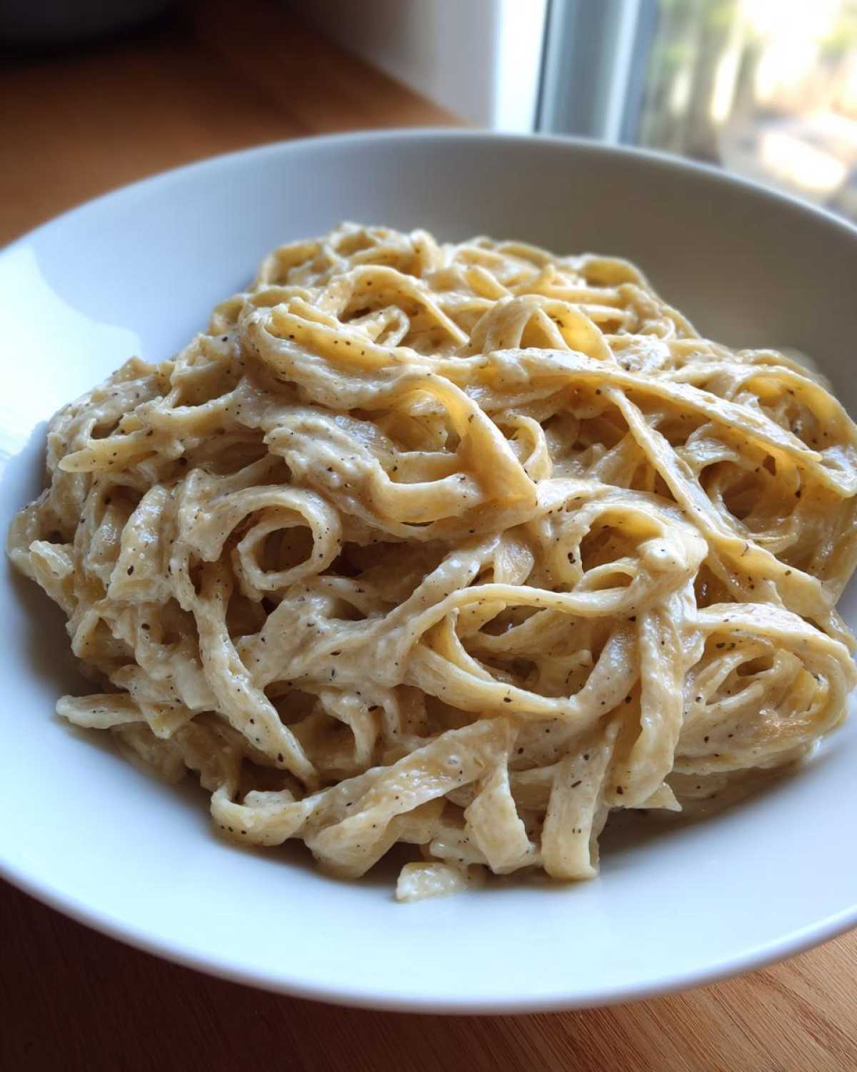 Close-up of fettuccine pasta generously coated in Vegan Creamy Cashew Alfredo Sauce, speckled with black pepper.