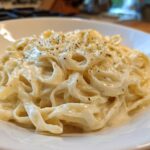 Close-up of fettuccine pasta generously coated in rich Vegan Creamy Cashew Alfredo Sauce and sprinkled with herbs.