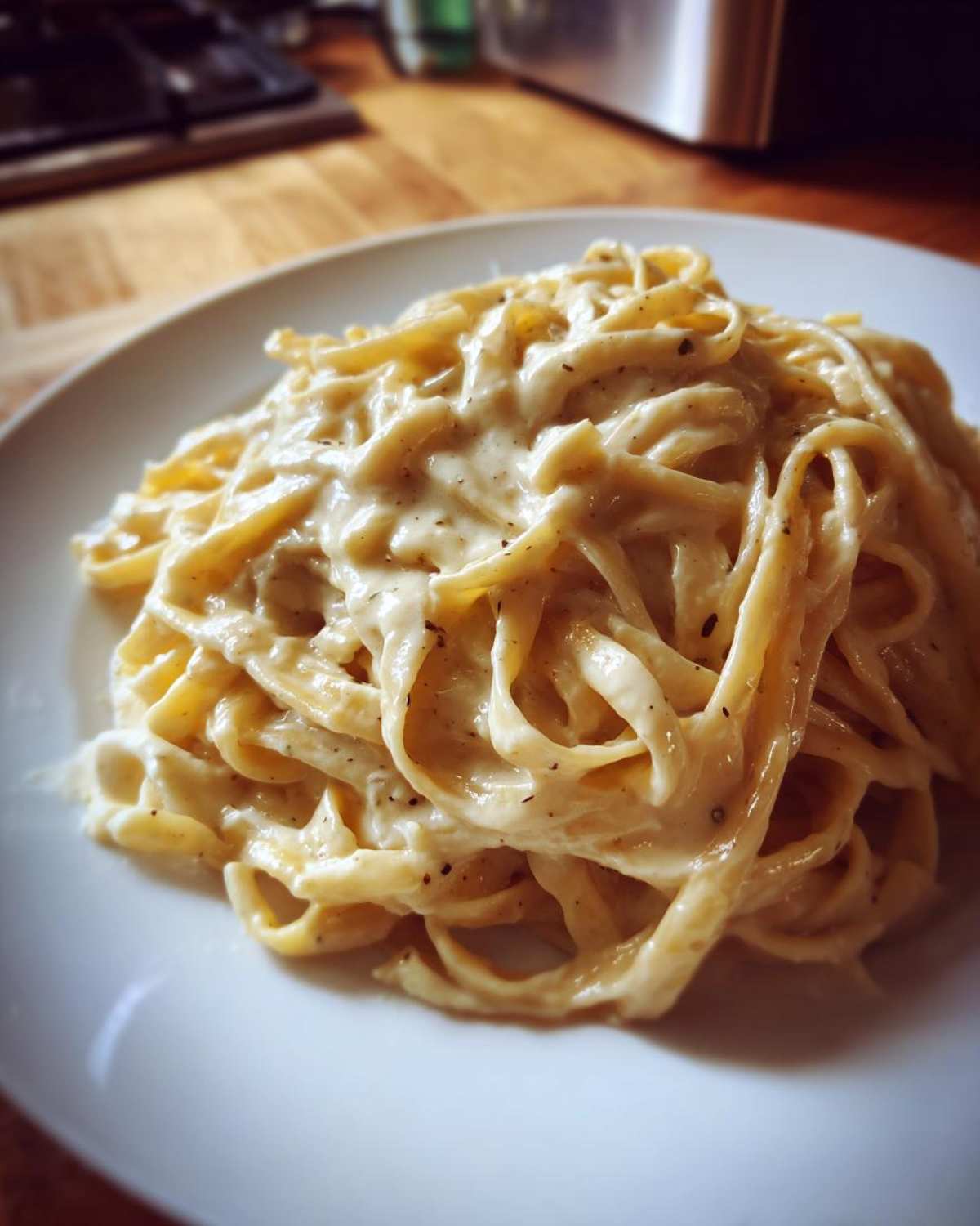 Close-up of fettuccine pasta generously coated in Vegan Creamy Cashew Alfredo Sauce on a white plate.