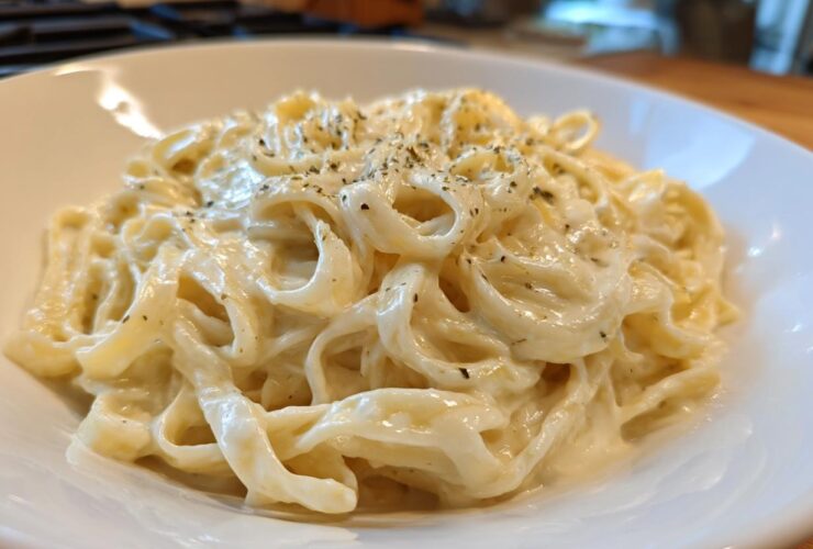 Close-up of fettuccine pasta generously coated in rich Vegan Creamy Cashew Alfredo Sauce and sprinkled with herbs.