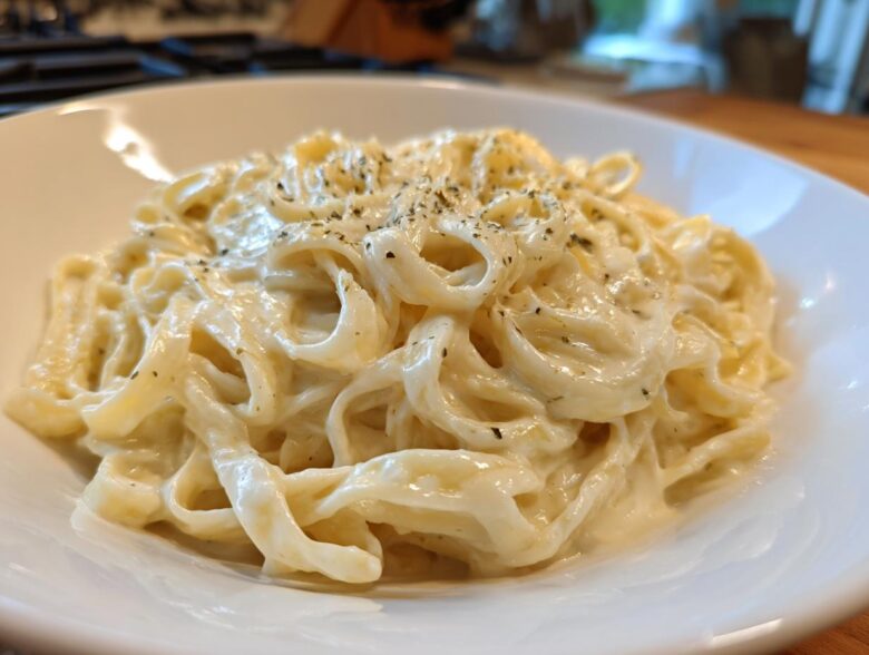 Close-up of fettuccine pasta generously coated in rich Vegan Creamy Cashew Alfredo Sauce and sprinkled with herbs.