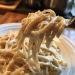Close-up of fettuccine noodles coated thickly in Vegan Creamy Cashew Alfredo Sauce, lifted by a fork.