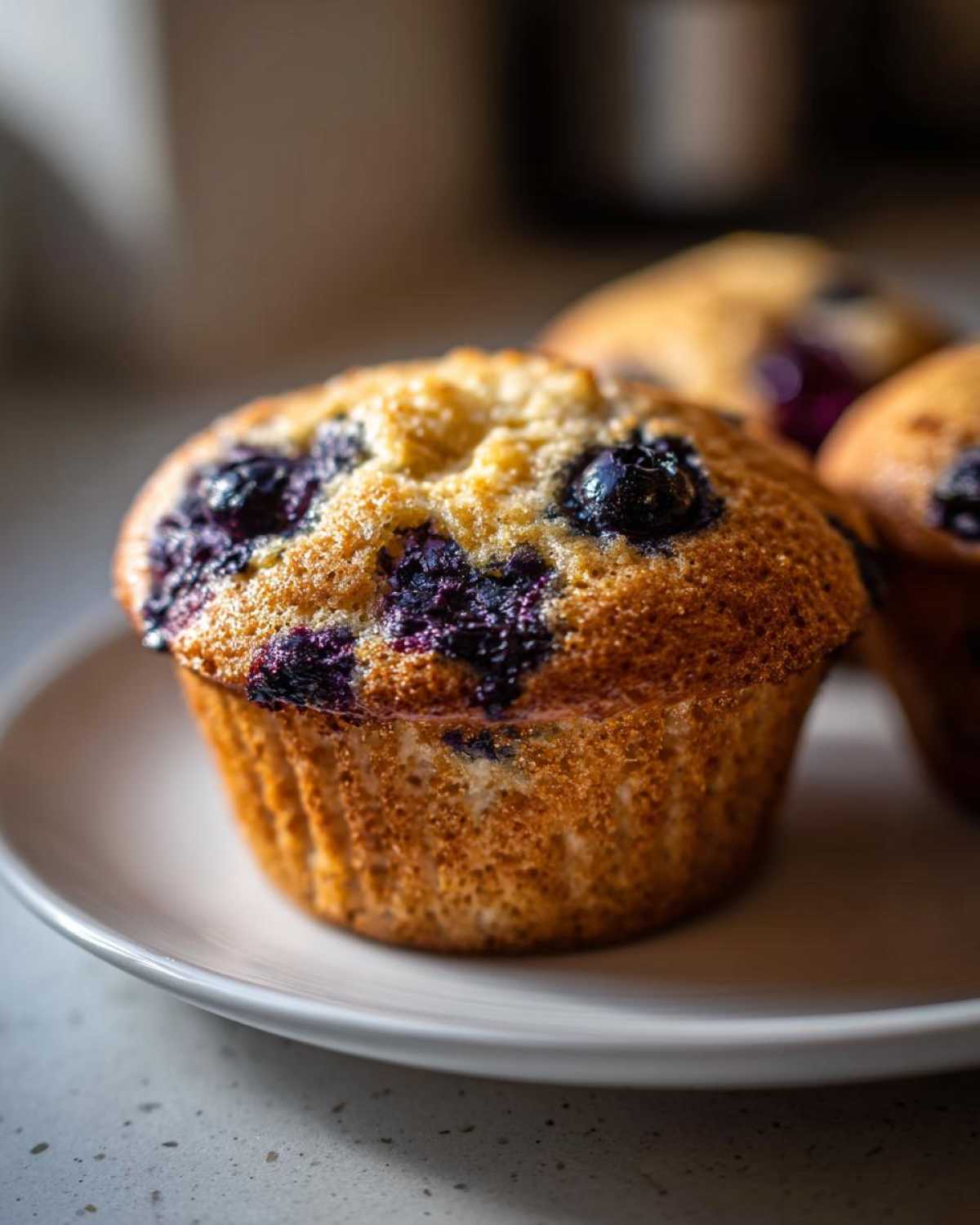 A close-up, appetizing shot of a golden-brown Vegan Lemon Blueberry Muffin topped with burst blueberries.