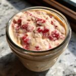 Close-up of Vegan Strawberry Cream Overnight Oats mixed with chunks of bright red strawberries in a glass jar.