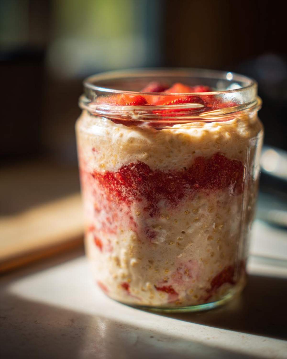 Close-up of Vegan Strawberry Cream Overnight Oats layered in a clear glass jar, topped with fresh strawberries.