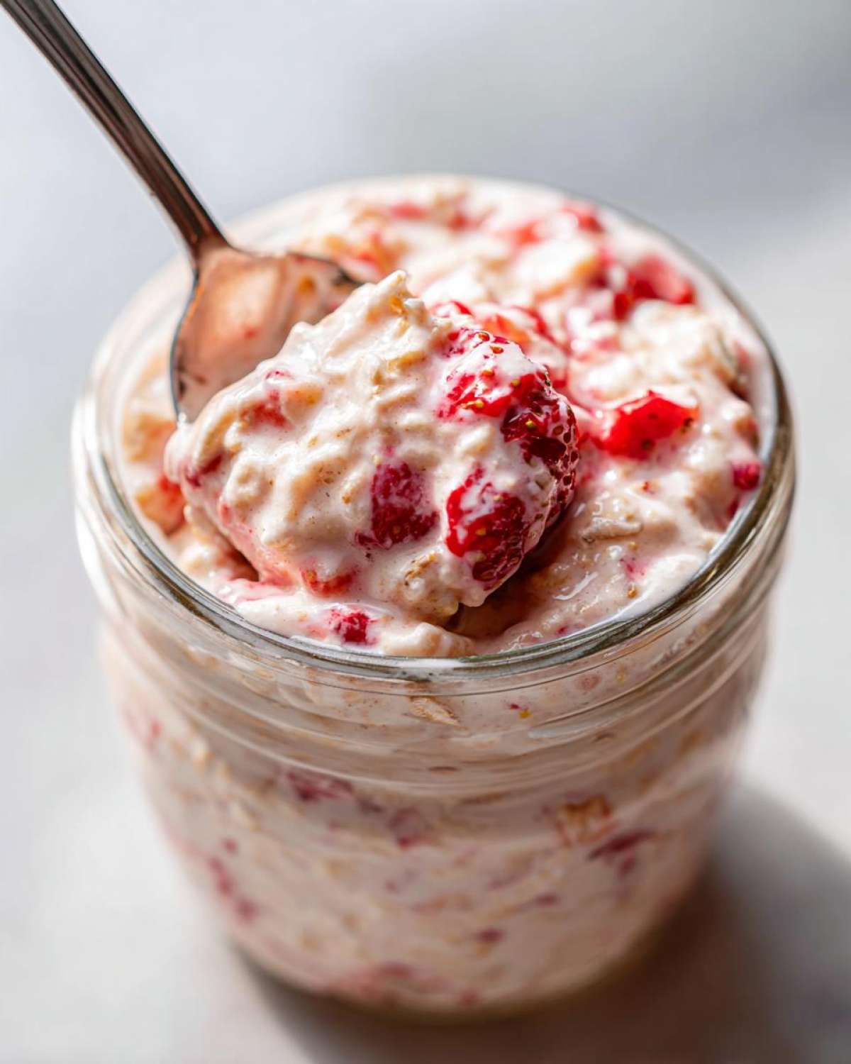 A spoonful of creamy Vegan Strawberry Cream Overnight Oats being lifted from a glass jar.