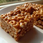Close-up of three square portions of sticky, caramel-colored cheerio bars resting on a white plate.