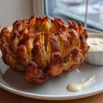 A perfectly cooked, crispy Air Fryer Blooming Onions served on a white plate next to a small bowl of creamy dipping sauce.