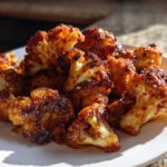 A close-up of glossy, caramelized Air Fryer Crispy BBQ Cauliflower Bites piled on a white plate.
