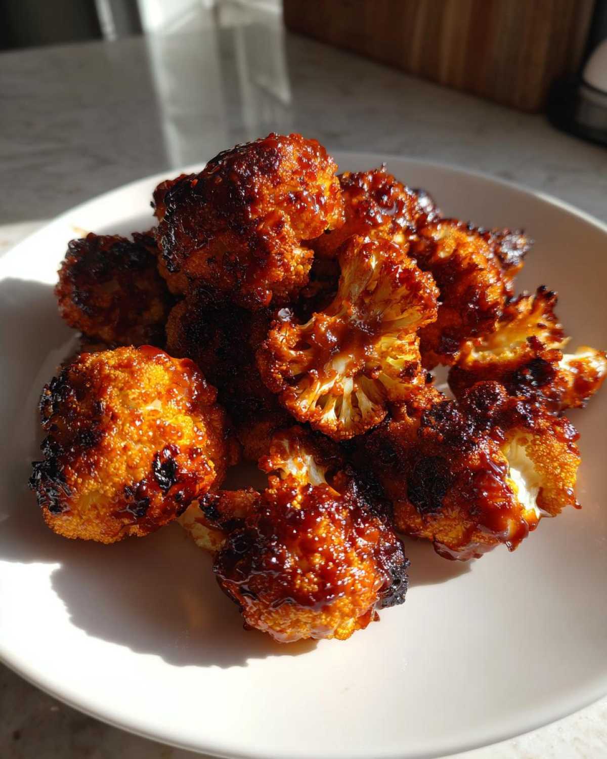 A close-up of a pile of glossy, caramelized Air Fryer Crispy BBQ Cauliflower Bites served on a white plate.