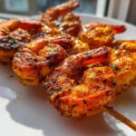 Close-up of perfectly cooked Air Fryer Crispy Cajun Shrimp Skewers resting on a white plate, showing vibrant seasoning.