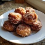 A stack of golden brown Air Fryer Crispy Cinnamon Sugar Biscuit Bites heavily coated in sparkling cinnamon sugar on a white plate.
