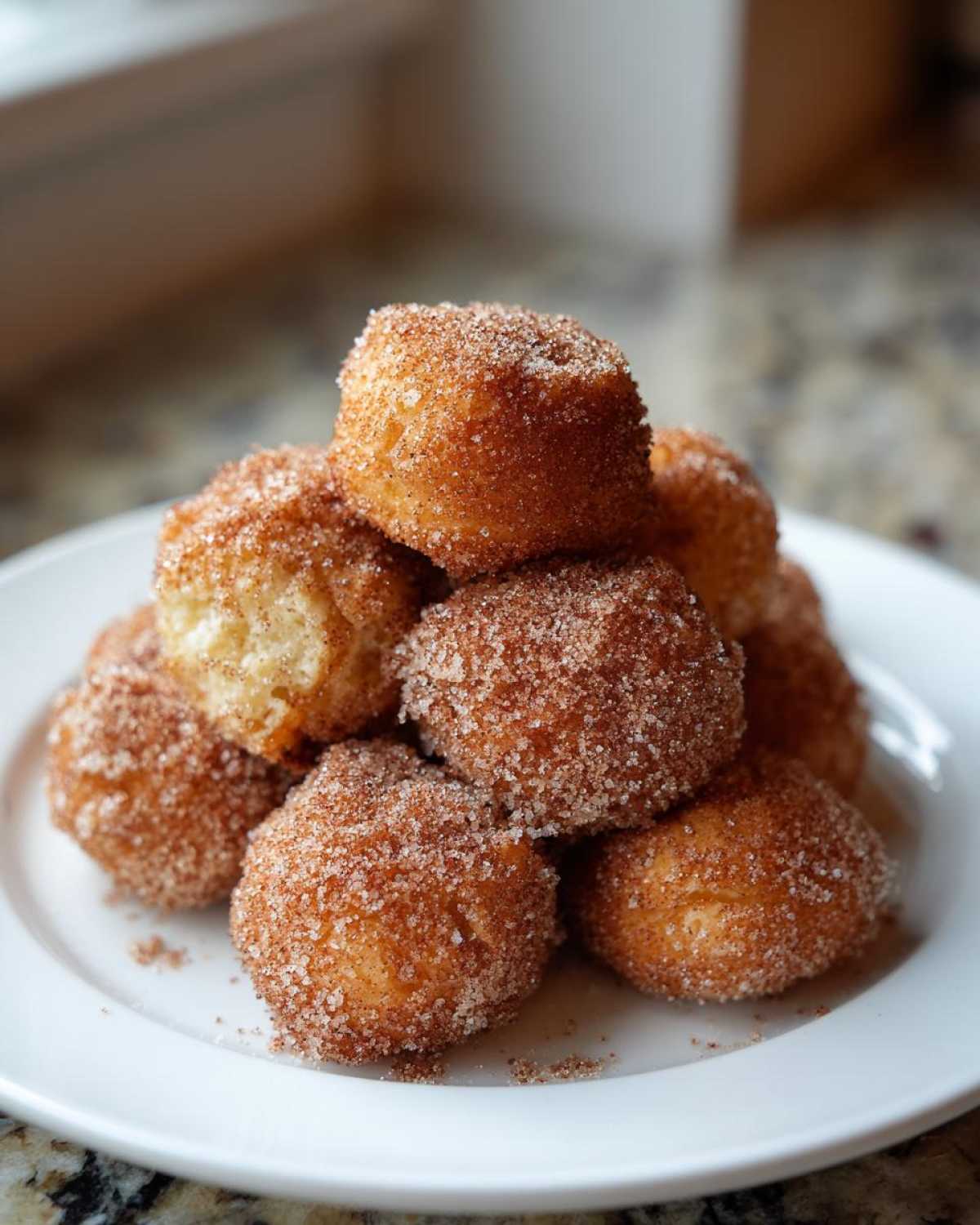 A stack of golden brown Air Fryer Crispy Cinnamon Sugar Biscuit Bites coated heavily in cinnamon sugar on a white plate.