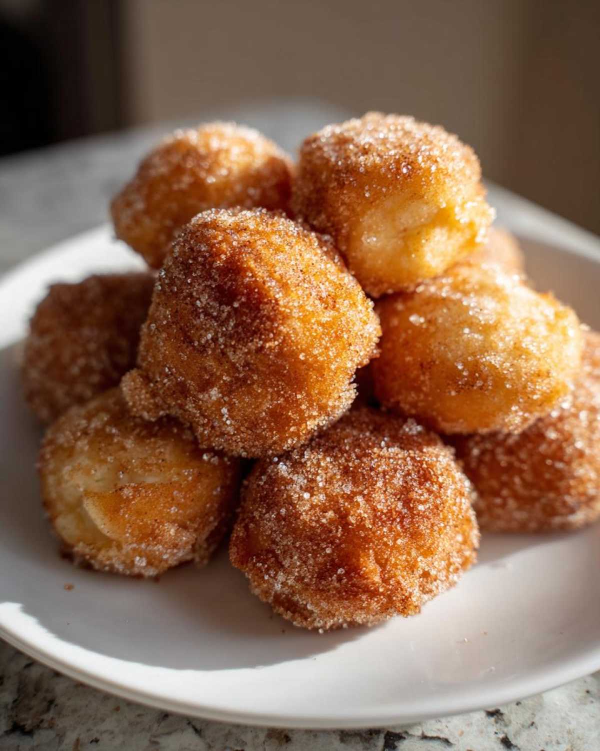 A stack of golden brown Air Fryer Crispy Cinnamon Sugar Biscuit Bites coated heavily in sparkling cinnamon sugar.