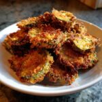 Close-up of golden brown, crispy Air Fryer Crispy Garlic Dill Pickles piled high on a white plate.