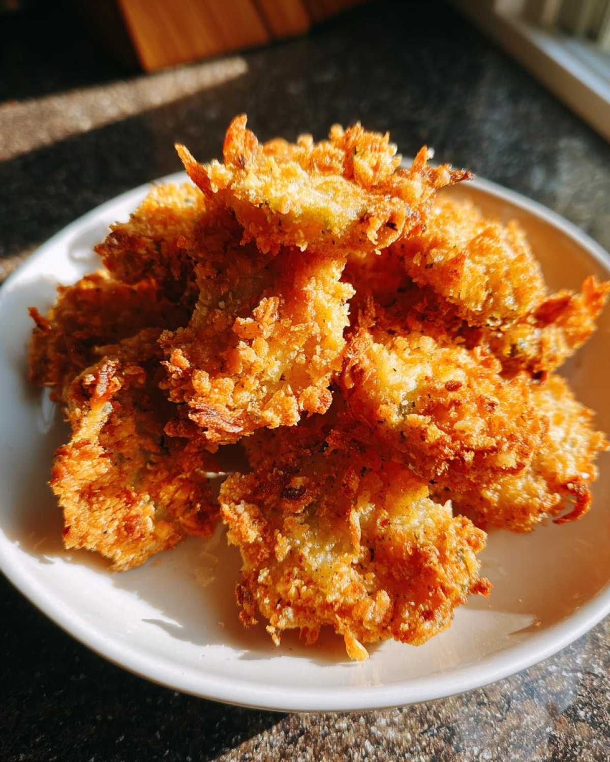 A pile of golden brown, crispy Air Fryer Crispy Garlic Dill Pickles served on a white plate.