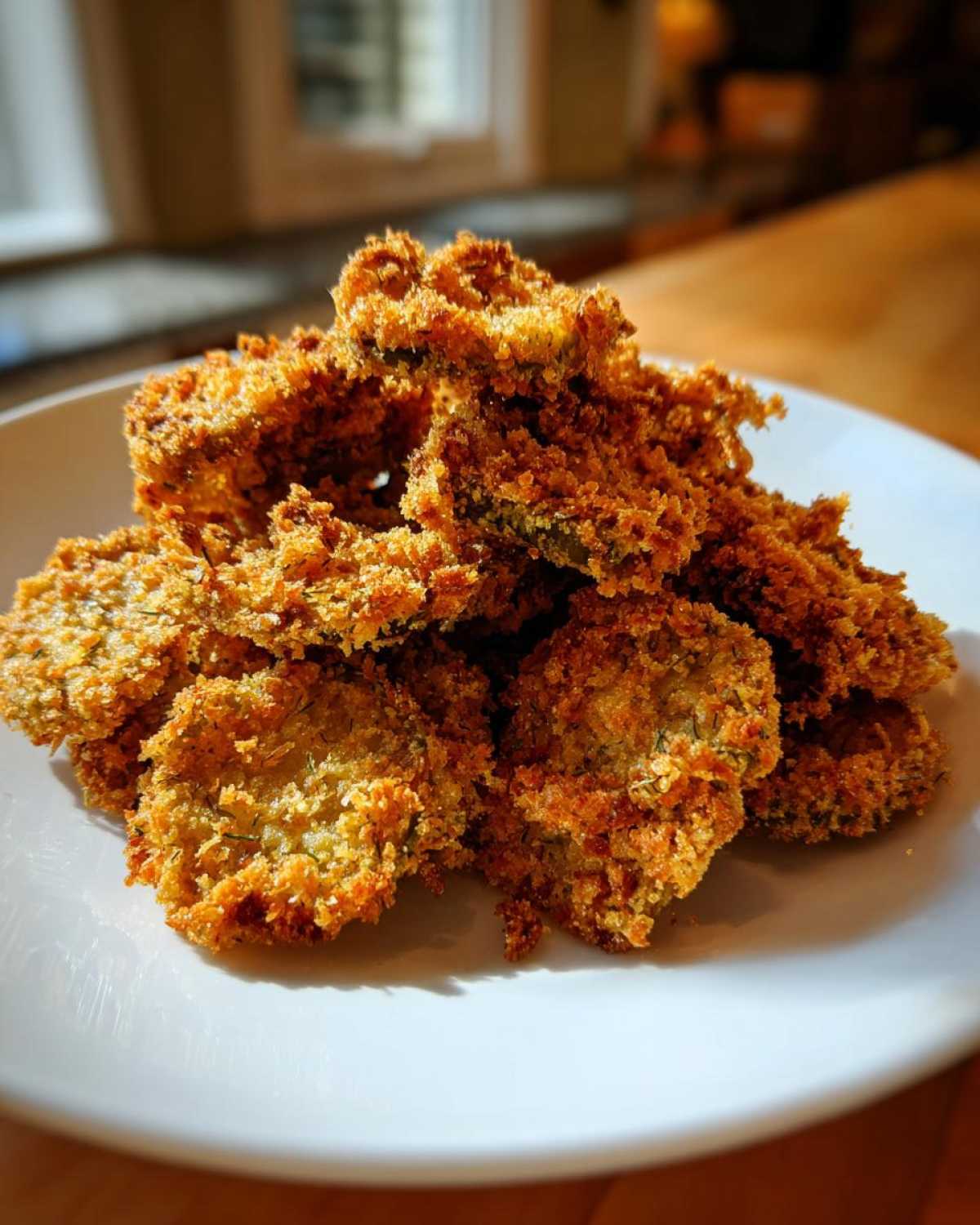 A mound of golden brown, crispy Air Fryer Crispy Garlic Dill Pickles piled high on a white plate.