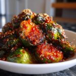 Close-up of Air Fryer Crispy Gochujang Brussels Sprouts coated in a spicy red glaze and sprinkled with sesame seeds.