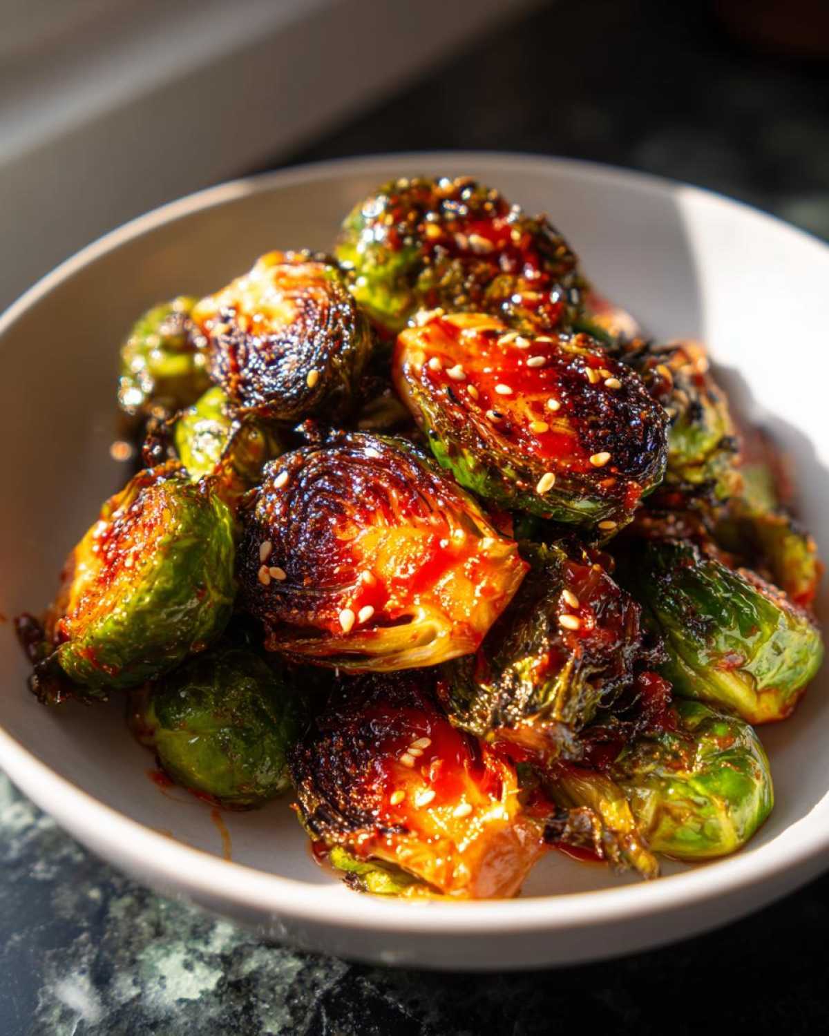 Close-up of crispy Air Fryer Crispy Gochujang Brussels Sprouts coated in a shiny red glaze and sprinkled with sesame seeds.