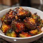 Close-up of crispy Air Fryer Crispy Gochujang Brussels Sprouts coated in spicy glaze and topped with sesame seeds.