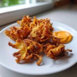Golden brown Air Fryer Crispy Onion Petals served on a white plate next to a dollop of orange spicy mayo.