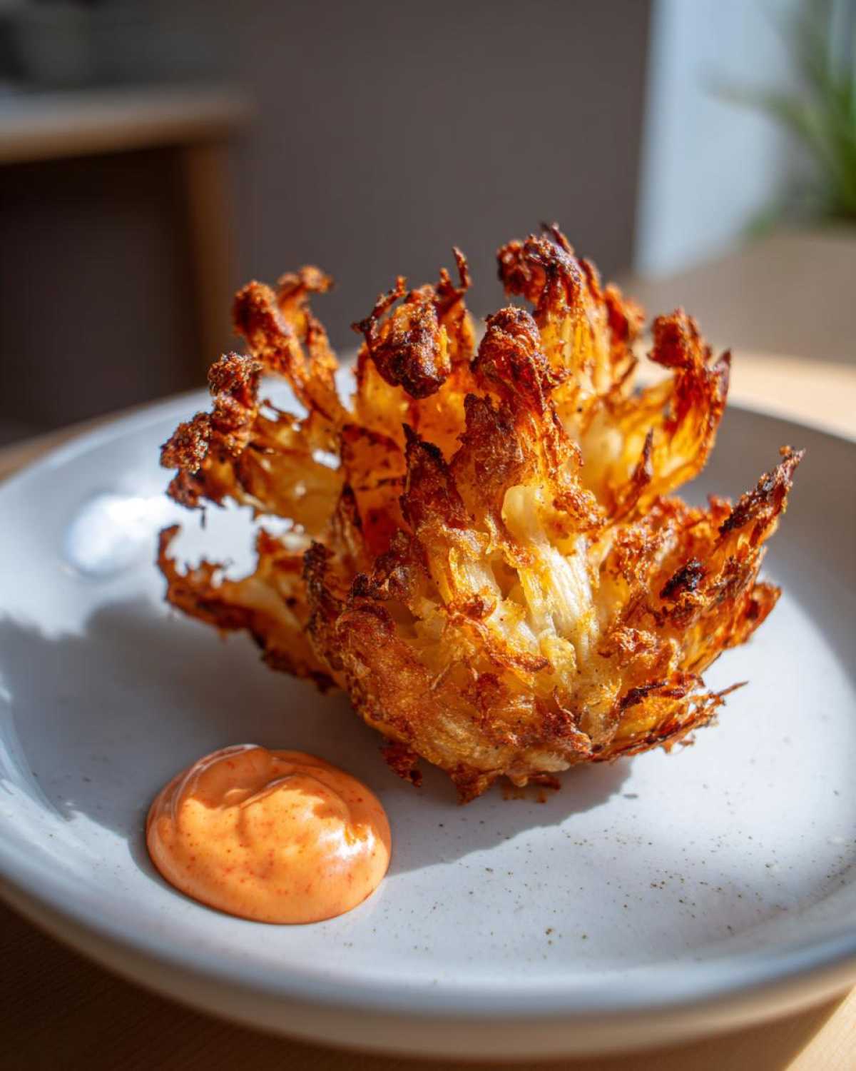 A perfectly cooked Air Fryer Crispy Onion Petals served on a plate next to a dollop of spicy mayo.