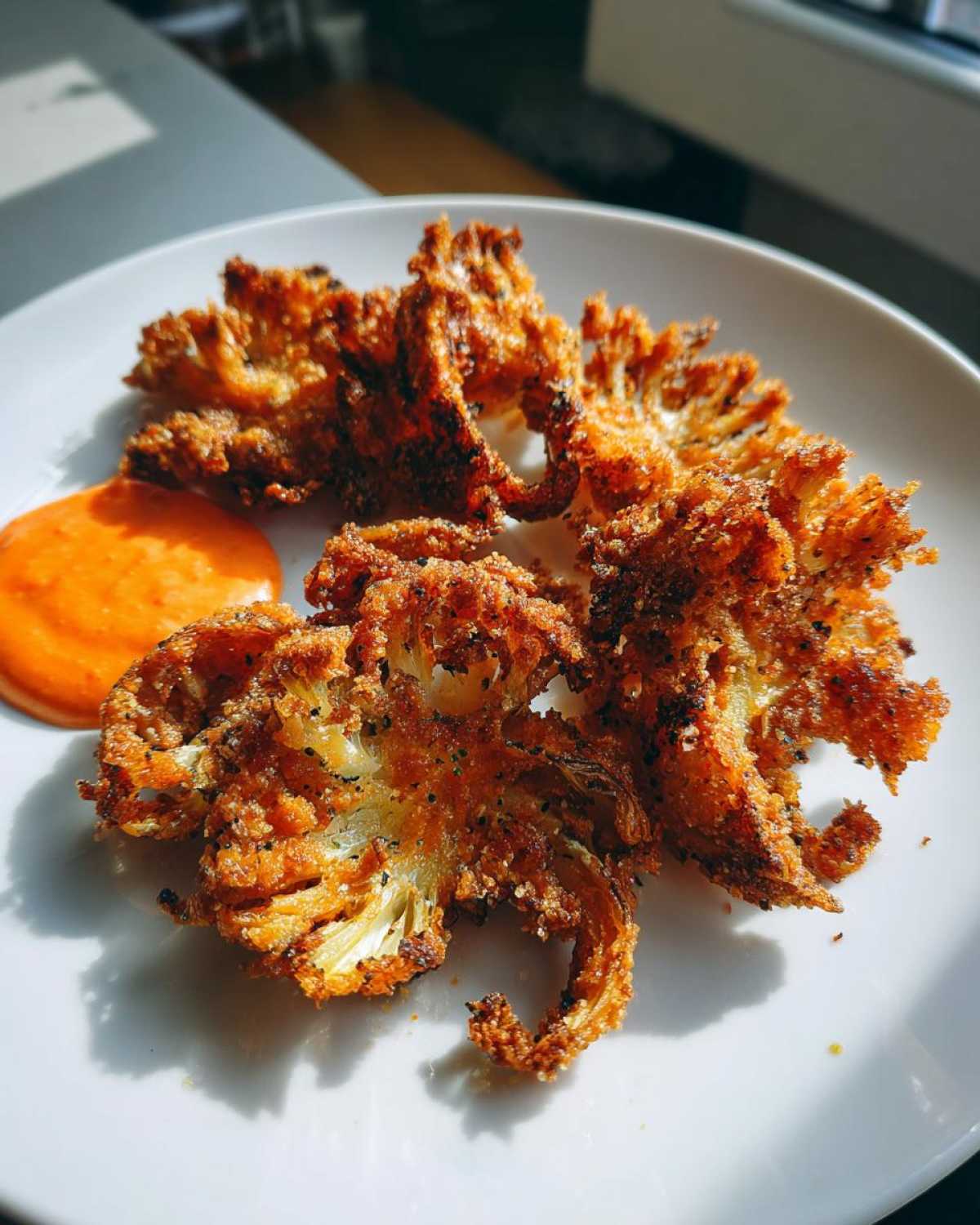 Close-up of golden brown Air Fryer Crispy Onion Petals served with a side of bright orange spicy mayo dip.