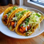 Three crispy tacos filled with spiced sweet potato chunks, shredded cabbage, and drizzled with white sauce.