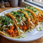 Four fully loaded Air Fryer Crispy Sweet Potato Tacos with bright orange filling, shredded cabbage, and cilantro on a white plate.