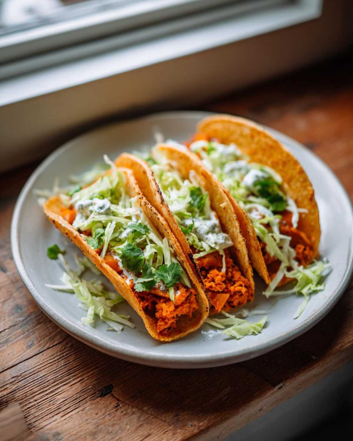 Three crispy tacos filled with orange sweet potato mash, shredded cabbage, and a creamy sauce, ready to eat.