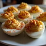 A plate of perfectly prepared deviled eggs, piped high with creamy filling and sprinkled with paprika.