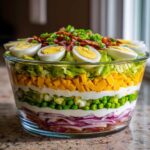 A tall, clear glass bowl showcasing a vibrant 7 layer salad with distinct layers of bacon, red onion, peas, cheese, lettuce, and topped with eggs.