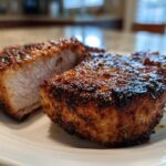 Two thick, juicy air fryer pork chops with a dark, caramelized crust resting on a white plate.