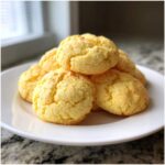 A stack of soft, yellow cake mix cookies piled high on a white plate, ready to eat.