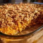 A close-up view of a freshly baked pumpkin crisp showing the bright orange filling and crunchy oat topping.