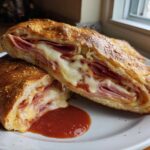A cross-section of a freshly baked Stromboli, revealing layers of deli meats and gooey, melted cheese, served with marinara sauce.