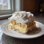 A square serving of THE BANANA PUDDING layered with vanilla custard, sliced bananas, and topped with piped whipped cream.