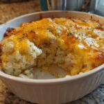 A close-up of a portion of baked Angel Chicken Rice Casserole in a white dish, topped with melted cheddar cheese and herbs.