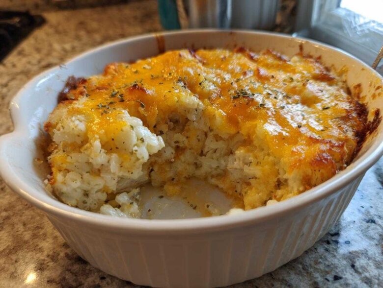 A close-up of a portion of baked Angel Chicken Rice Casserole in a white dish, topped with melted cheddar cheese and herbs.