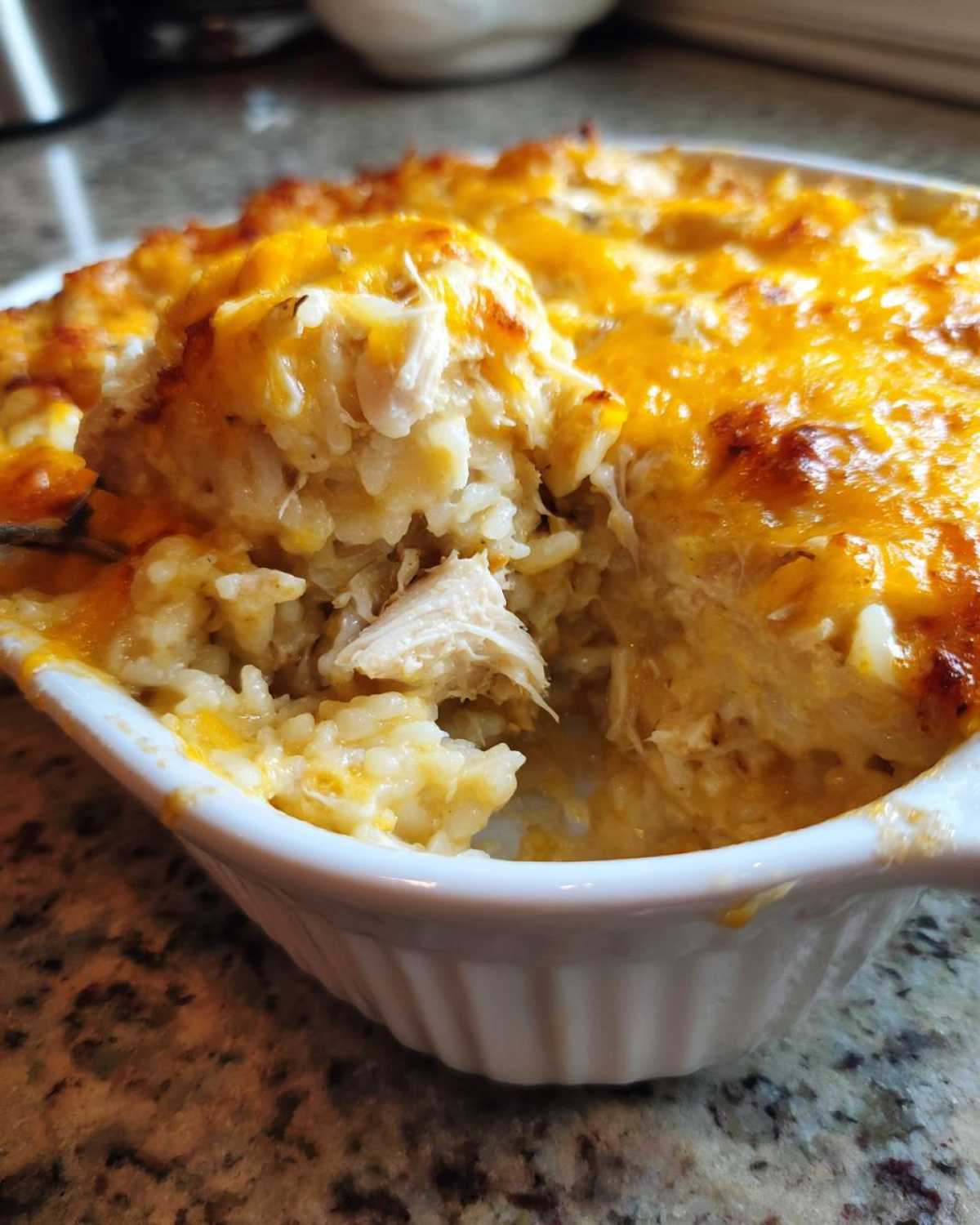 A spoonful being lifted from a white ramekin showing creamy Angel Chicken Rice Casserole topped with melted, bubbly cheddar cheese.