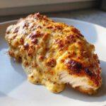 A close-up of a juicy Baked Caesar Chicken smothered in a rich, bubbly Baked Caesar Chicken Creamy Parmesan Sauce.